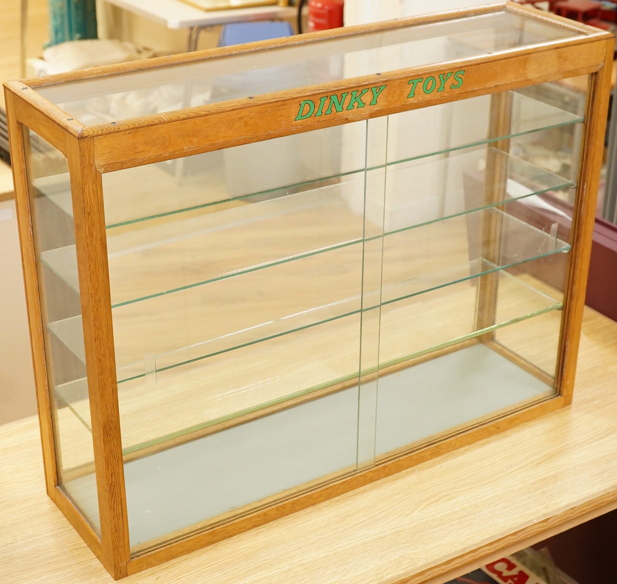 A Dinky Toys glazed oak shop counter retail display cabinet, this is the more scarce ‘front loading’ version of this cabinet, with ‘Dinky Toys’ in green to the top bar, height 61cm, width 81cm, depth 23cm